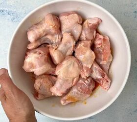 crispy salt and vinegar chicken wings recipe, A hand holds a white bowl filled with raw marinated chicken drumettes placed on a light blue surface