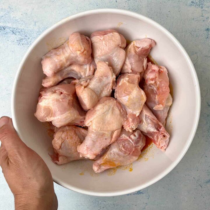 crispy salt and vinegar chicken wings recipe, A hand holds a white bowl filled with raw marinated chicken drumettes placed on a light blue surface