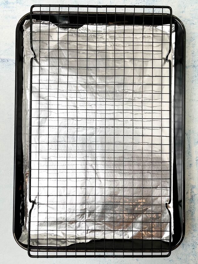 crispy salt and vinegar chicken wings recipe, A baking tray lined with aluminum foil topped with a black wire cooling rack The tray is set on a light blue surface