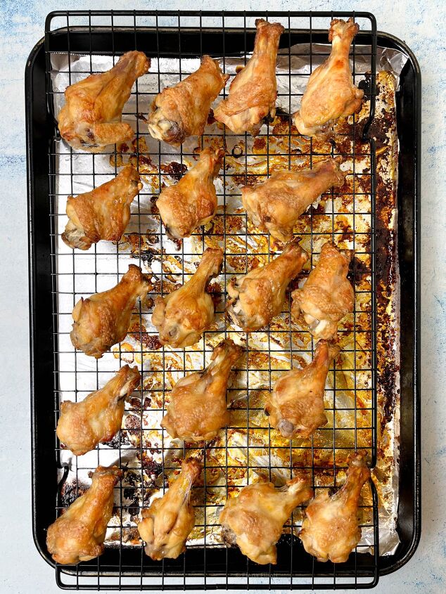 crispy salt and vinegar chicken wings recipe, Golden brown chicken drumettes arranged evenly on a wire rack over a foil lined baking tray The tray shows some oil and seasoning residue indicating they are freshly baked The background is a light blue surface