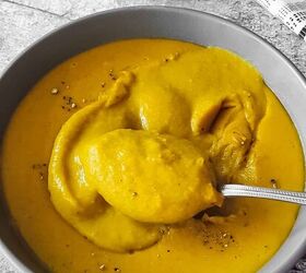 curried lentil carrot soup, Thick and creamy deep yellow color lentil soup with some crushed black pepper garnish is being scooped up with a spoon