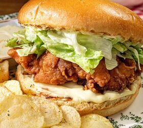 buttermilk crispy chicken sandwich, A crispy fried chicken sandwich with lettuce and mayonnaise is on a decorative plate The sandwich is accompanied by potato chips The plate is set on a wooden table with a bowl of chips in the background
