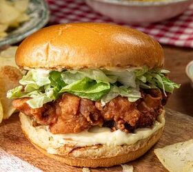 buttermilk crispy chicken sandwich, A crispy fried chicken sandwich with shredded lettuce and mayonnaise on a brioche bun sits on a wooden board surrounded by potato chips A small dish of dipping sauce is nearby and a bowl with a red and white checkered cloth is in the background