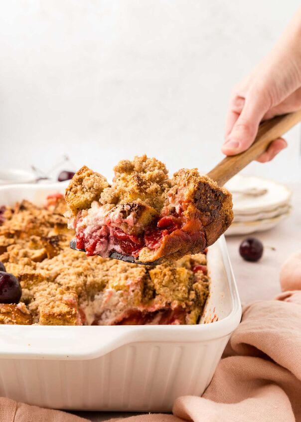 cherry cheesecake french toast casserole, a spoonful of casserole being lifted out of white baking dish