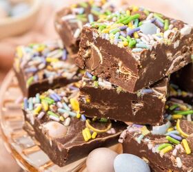 easter fudge, A stack of chocolate fudge cubes on a glass plate topped with colorful sprinkles and small candy eggs A soft focus bowl of candies is in the background with a pastel pink napkin nearby