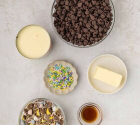 easter fudge, Ingredients for a recipe on a light surface include a bowl of chocolate chips a dish of butter a glass of vanilla extract a bowl of colorful sprinkles crumbled chocolate eggs and an open can of condensed milk