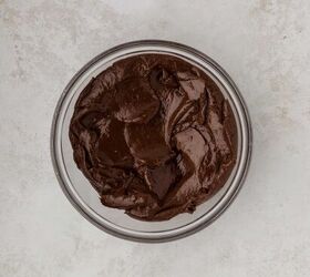 easter fudge, A glass bowl filled with smooth dark chocolate frosting sits on a textured light gray surface