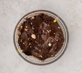 easter fudge, A glass bowl filled with dark chocolate mixed with chocolate eggs placed on a light gray marble surface