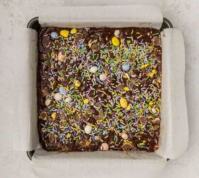 easter fudge, A square pan filled with chocolate fudge topped with colorful sprinkles and small pastel eggs The pan is lined with parchment paper set on a light colored countertop