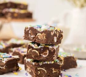 easter fudge, A stack of three pieces of chocolate fudge topped with colorful sprinkles and embedded with chunks of chocolate eggs More fudge pieces are blurred in the background with a soft focus on light tableware and a plant