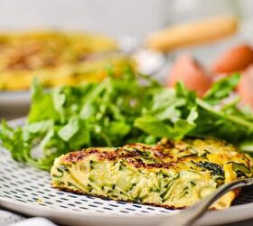 spanish zucchini tortilla, Side view of a slice of zucchini tortilla de patatas on a plate with a green salad on the side