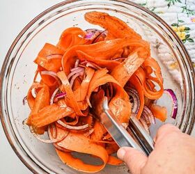 spicy carrot feta galette, Using tongs to mix together the carrot ribbons onions and spices