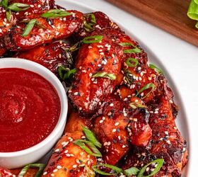 easy slow cooker korean chicken wings recipe, Crispy Korean chicken wings topped with sesame seeds and green onions served on a white plate with a bowl of sauce