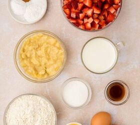 strawberry banana pancake casserole, Ingredients for baking are arranged on a light surface chopped strawberries flour mashed bananas milk two eggs melted butter vanilla extract sugar and small bowls of baking powder baking soda and cinnamon