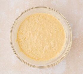 strawberry banana pancake casserole, A clear glass bowl filled with light yellow frothy batter sits on a textured light beige countertop The batter appears bubbly and smooth