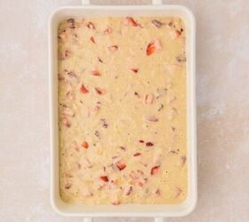 strawberry banana pancake casserole, A rectangular baking dish filled with a thick creamy pancake batter mixed with chopped red strawberries The dish rests on a light beige textured surface