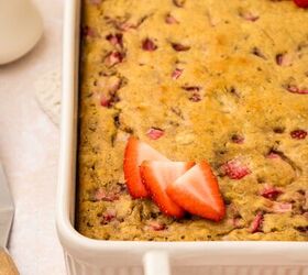 strawberry banana pancake casserole, Close up of a rectangular strawberry banana pancake casserole in a white dish The casserole is golden brown with pieces of strawberries visible Sliced strawberries garnish the top A knife and cup are seen in the blurred background