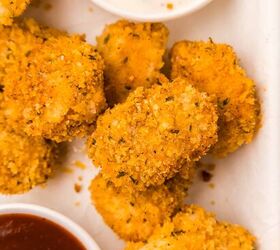 oven baked chicken nuggets, Golden crispy chicken nuggets with a seasoned breadcrumb coating are arranged next to two dipping sauces one is a creamy white ranch and the other is a rich dark red bbq sauce The scene is set on a white surface