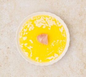 oven baked chicken nuggets, A white round dish contains melted butter with small solidified bits on the surface and a piece of raw chicken in the center The background is light and textured