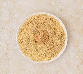 oven baked chicken nuggets, A white plate filled with finely ground breadcrumbs is set against a light beige textured background The breadcrumbs are light brown and evenly spread on the plate with a piece of chicken in the middle