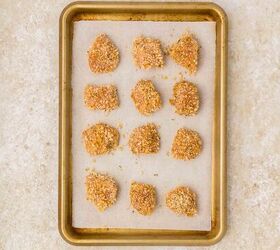 oven baked chicken nuggets, A baking tray lined with parchment paper holds twelve uncooked breaded chicken nuggets They are evenly spaced and placed on a light colored countertop