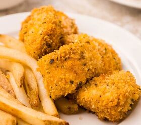 oven baked chicken nuggets, A white plate with golden brown breaded chicken nuggets and a serving of French fries A bowl of dipping sauce is blurred in the background