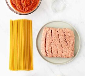 ground turkey with spaghetti, Ingredients for a pasta dish arranged on a white surface uncooked spaghetti ground meat on a plate a bowl of tomato sauce diced onions mixed dried spices and a small bowl of water