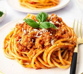 ground turkey with spaghetti, A plate of spaghetti topped with ground turkey grated cheese and fresh basil with a black and gold fork on the side Another plate of pasta is visible in the background