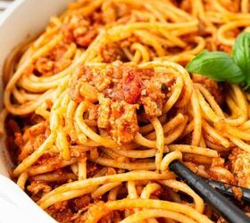 ground turkey with spaghetti, Close up of spaghetti coated in a chunky tomato and meat sauce served in a white bowl with a black serving spoon and a sprig of fresh basil for garnish