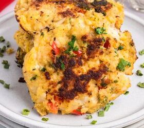 classic crab cake recipe little filler, A close up of two golden brown crab cakes with visible herbs and red pepper pieces served on a white plate