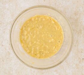 cake mix banana bread, A clear glass bowl filled with a smooth creamy cake mix banana bread batter rests on a light speckled countertop The batter is pale yellow and slightly lumpy indicating the presence of mashed bananas
