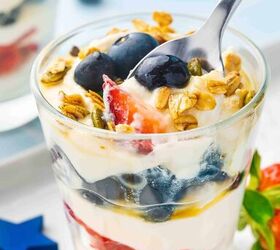 summer berry ricotta parfait easy 4th of july dessert, Close up side angle of a spoon scooping red strawberries blue blueberries creamy ricotta and granola from a patriotic summer parfait