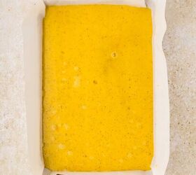 sheet pan eggs, A rectangular baking pan lined with white parchment paper is filled with whisked eggs speckled with tiny dots and set on a light beige surface