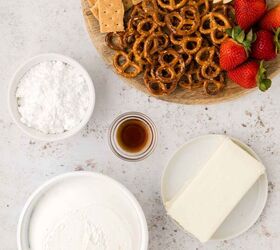 cool whip fruit dip, A wooden board with graham crackers apple slices pretzels and strawberries next to bowls of powdered sugar vanilla extract cream cheese and a bowl of cool whip on a light surface