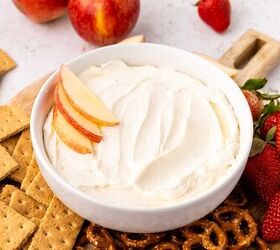 cool whip fruit dip, A bowl of creamy cool whip dip topped with apple slices is surrounded by graham crackers pretzels fresh strawberries and whole apples on a wooden board