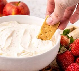 cool whip fruit dip, A hand dips a graham cracker into a bowl of creamy cool whip dip surrounded by fresh strawberries apples and pretzels on a wooden board