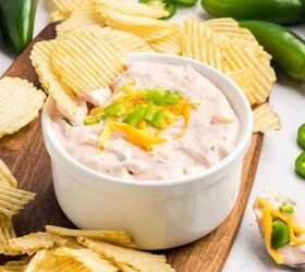salsa and cream cheese dip, A white bowl of creamy dip topped with shredded cheese and chopped jalape os is surrounded by ridged potato chips on a wooden board with fresh jalape os scattered nearby