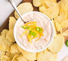 salsa and cream cheese dip, A bowl of creamy dip topped with shredded cheddar cheese and chopped green onion is surrounded by crinkle cut potato chips on a wooden board with jalape o peppers nearby