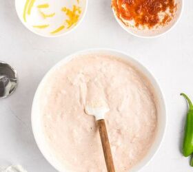 salsa and cream cheese dip, A mixing bowl with a creamy pale pink dip a spatula a bowl with shredded cheese a bowl with salsa a metal mixer and a jalape o on a white surface