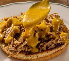 sweet and tangy carolina bbq sauce mustard based classic, A spoon pours yellow sauce over shredded meat on a toasted sandwich bun placed on a white plate with a green rim