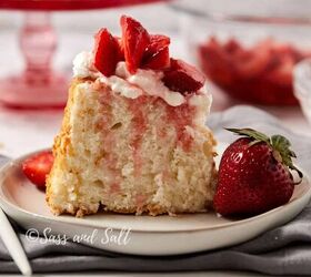 easy peach cobbler pound cake with brown butter glaze, A slice of light airy cake topped with whipped cream and fresh strawberry slices is served on a white plate A whole strawberry is positioned beside the cake slice The background includes a bowl of sliced strawberries and a red cake stand Credit Sass and Salt