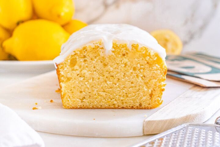 starbucks copycat lemon loaf, A sliced Starbucks copycat lemon loaf with white icing sits on a marble board with fresh lemons in the background