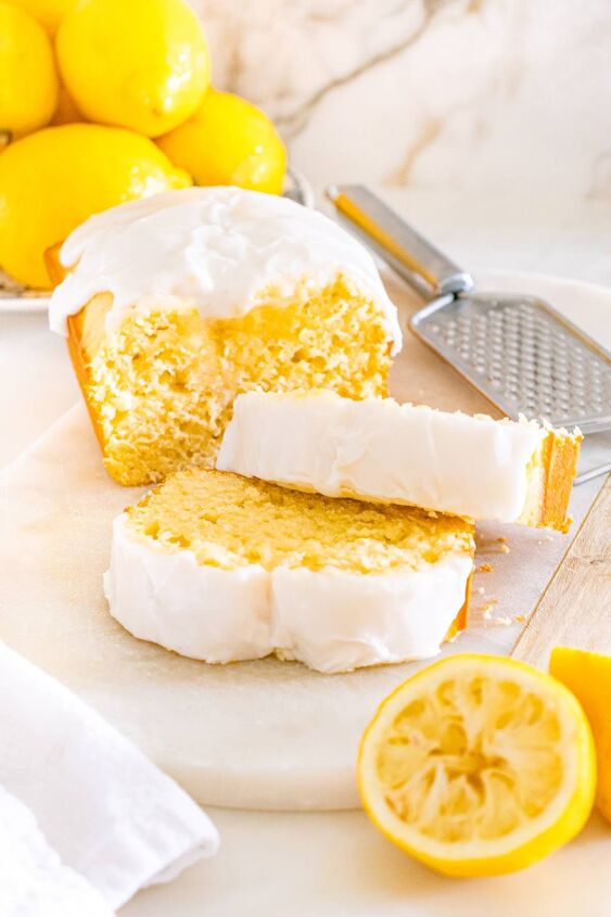 starbucks copycat lemon loaf, A lemon loaf cake with white icing sliced surrounded by fresh lemons and a zester on a marble surface