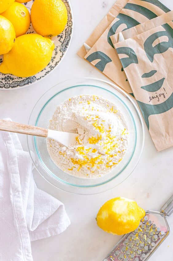 starbucks copycat lemon loaf, A bowl of flour and lemon zest with a spatula surrounded by lemons napkins and a white cloth