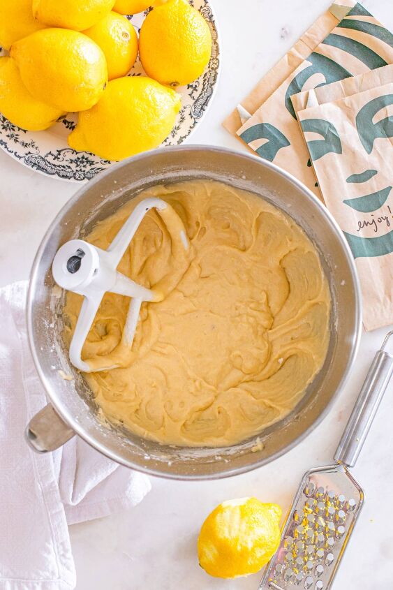 starbucks copycat lemon loaf, A mixing bowl with lemon cake batter surrounded by lemons a grater and paper bags on a countertop
