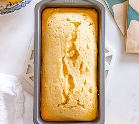 starbucks copycat lemon loaf, A loaf of lemon bread in a baking pan on a white surface surrounded by lemons and a kitchen towel