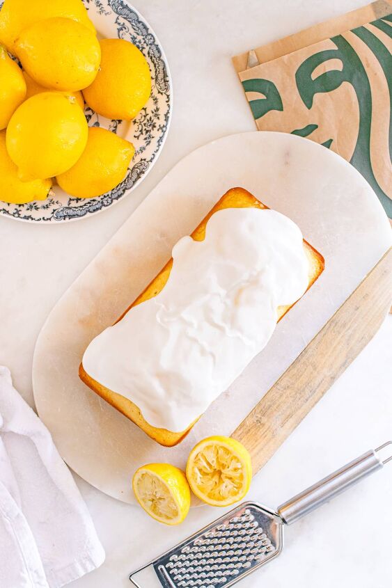 starbucks copycat lemon loaf, Iced lemon loaf on a board with whole and halved lemons a grater and a patterned plate nearby