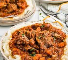 stracotto italian pot roast, A plate of mashed potatoes topped with beef stew in tomato sauce with carrots and herbs