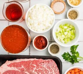 stracotto italian pot roast, Raw beef chopped vegetables spices tomato sauce broth and oil arranged on a white tiled surface