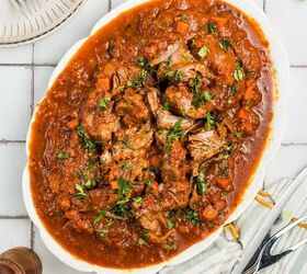 stracotto italian pot roast, A white plate with beef stew in tomato sauce garnished with herbs on a tiled table with utensils nearby